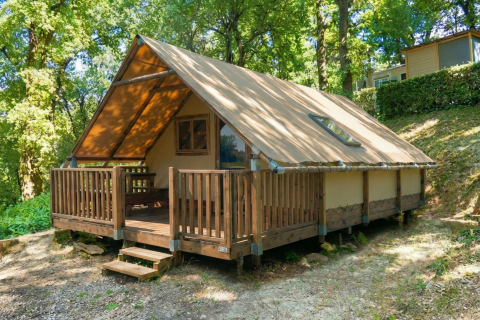 Tente Safari Lodge All Season avec terrasse en bois, située en pleine forêt, idéale pour un séjour en nature.