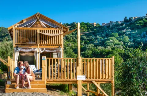 Famille assise devant un lodge en bois au Vallicella Glamping Resort en Toscane, entourée de collines vertes.