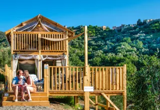 Famille assise devant un lodge en bois au Vallicella Glamping Resort en Toscane, entourée de collines vertes.
