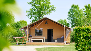 Tenda safari Nomad con veranda, barbecue e amaca, circondata dal verde e illuminata dalla luce del sole.