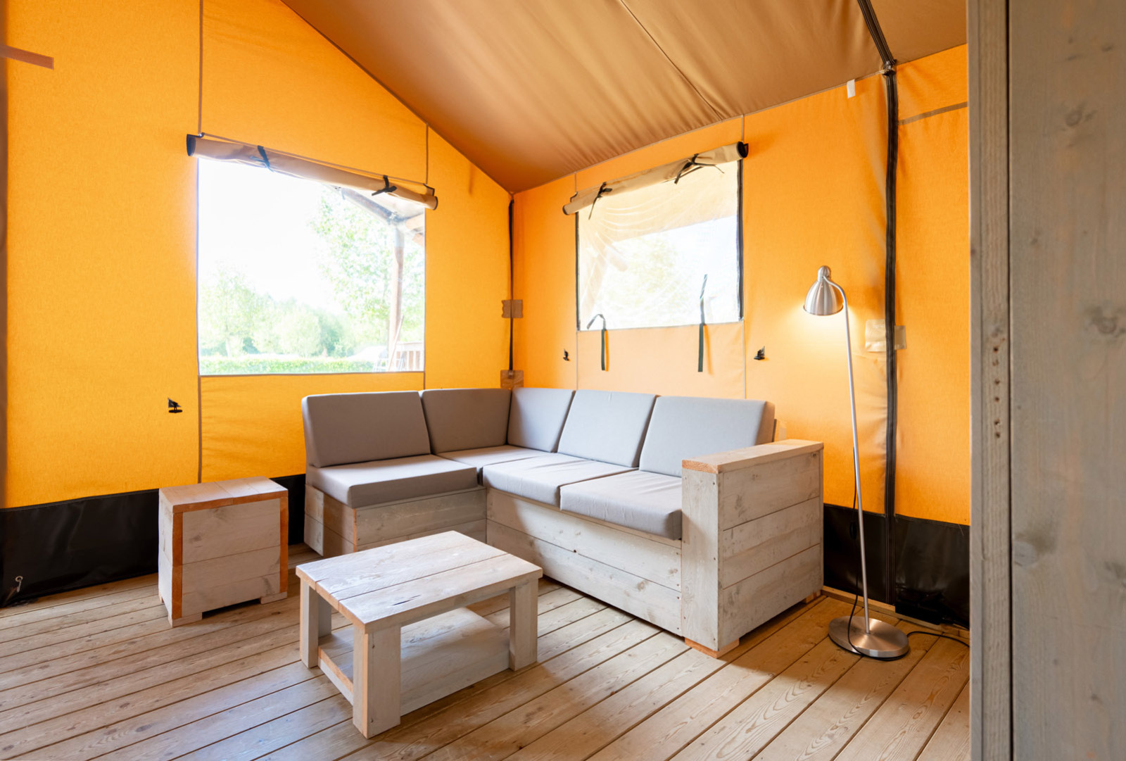 Interieur van safaritent 'Nomad' op Camping Le Moulin de Bel Air in Frankrijk met sofa, tafels en lamp.