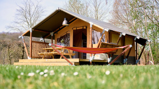 Safari-teltet Compact står på en græsplæne, med hængekøje, terrasse og havebord under åben himmel.