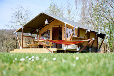 La tenda safari Compact si trova su un prato, con amaca, terrazza in legno e tavolo da picnic esterno.