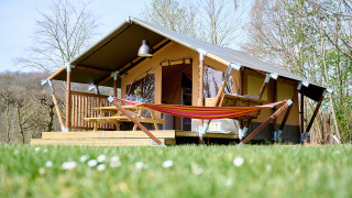 La tenda safari Compact si trova su un prato, con amaca, terrazza in legno e tavolo da picnic esterno.