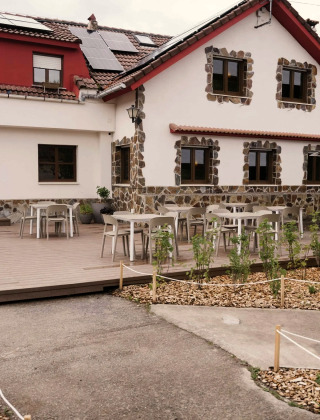 Buitenterras van Wecamp Cudillero vakantiepark in Asturië, Spanje, met tafels en stoelen bij een stenen huis.