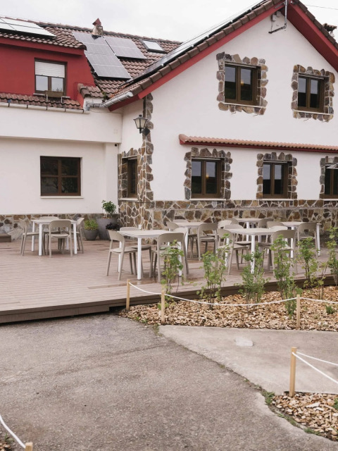 Außenterrasse im Wecamp Cudillero Ferienpark, Asturias, Spanien, mit Tischen und gemütlichem Steinhaus.