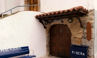 Entrance to a building in Cudillero, Asturias, Spain with a bench and signs that read Ribera and Pescaderia.