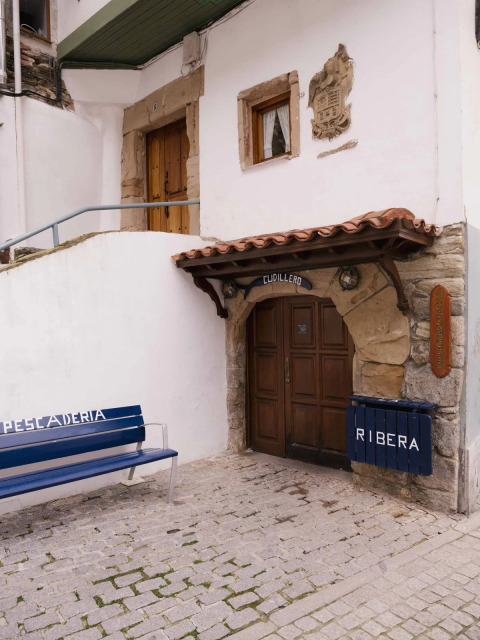 Eingang eines Gebäudes in Cudillero, Asturien, Spanien, mit Sitzbank und Schildern Ribera und Pescaderia.