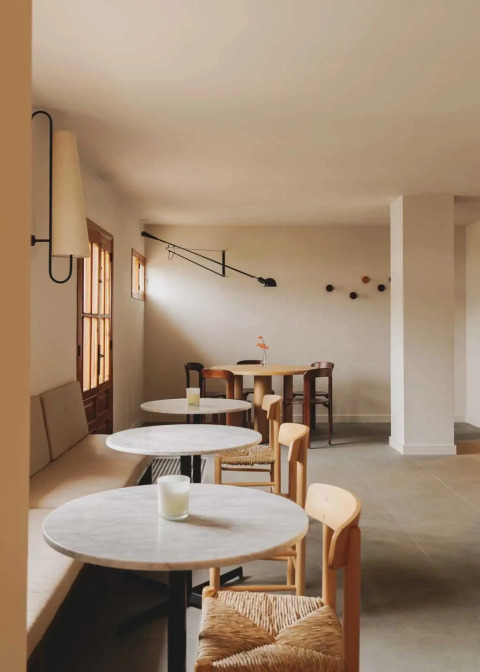 Heller, minimalistischer Cafébereich mit runden Tischen und Holzmöbeln in Wecamp Cudillero, Asturien.