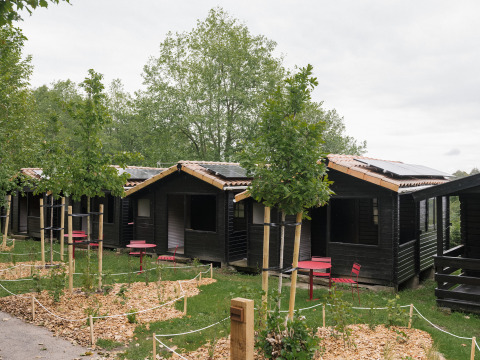 Kleine Holzhütten mit roten Stühlen und Tischen vor den Eingängen im Ferienpark Wecamp Cudillero, Asturias.