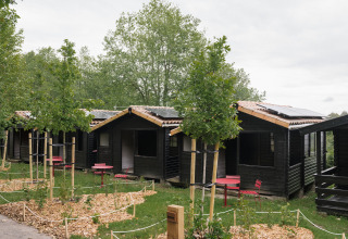 Kleine Holzhütten mit roten Stühlen und Tischen vor den Eingängen im Ferienpark Wecamp Cudillero, Asturias.