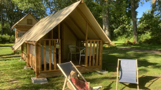 Tenda safari chiamata Insulated bivouac Rando con sedie fuori, circondata da alberi ed erba in una giornata di sole.
