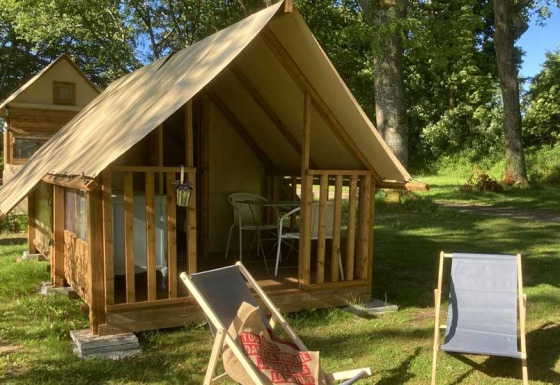 Safaritent genaamd Insulated bivouac Rando met stoelen buiten, omringd door bomen en gras op een zonnige dag.