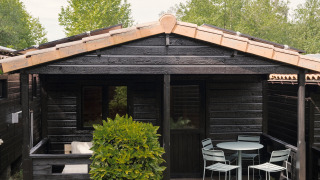 Black wooden bungalow with small patio, garden furniture, and greenery at Bungalow Basic Family Plus.
