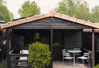 Schwarze Holzhütte mit Veranda, Gartenmöbeln und grüner Umgebung bei Bungalow Basic Family Plus.