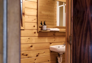 Kleines Badezimmer mit Holzvertäfelung, Waschbecken, WC und Spiegel in einer gemütlichen Glamping-Unterkunft.