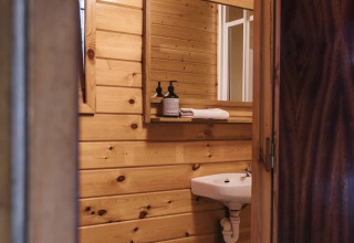 Baño pequeño con paredes de madera, lavabo, inodoro y espejo en un alojamiento de glamping acogedor.