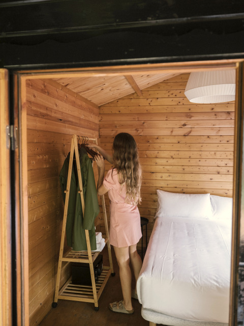 Woman in a pink dress organizes clothes in the cozy wood Bungalow Basic Couple at Wecamp Cudillero, Spain.