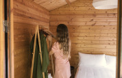 Woman in a pink dress organizes clothes in the cozy wood Bungalow Basic Couple at Wecamp Cudillero, Spain.