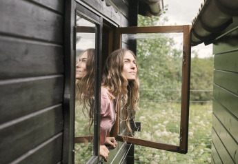 Woman looking out an open window of the black tiny house Bungalow «Basic Couple» at Wecamp Cudillero, Spain.