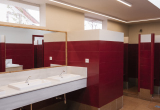 Salle de bain moderne avec carrelage rouge, double vasque et cabines ouvertes au Cottage Family Tent, Wecamp Cudillero, Espagne.