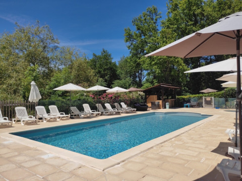 Outdoor pool at Campsite Pagel in Occitanie, France, with deck chairs and umbrellas under blue sky.