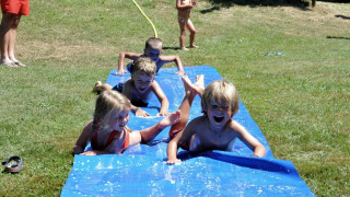 Kinder rutschen lachend auf einer Wasserrutsche auf einem Campingplatz in Occitanie, Frankreich, im Sommer.