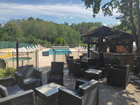 Zona lounge esterna con poltrone in vimini, piscina e bar, circondata da alberi a Catus, Occitania, Francia.