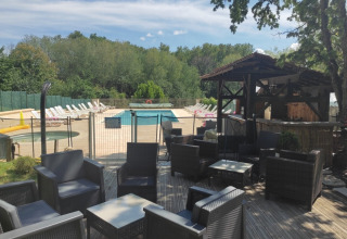 Zona lounge esterna con poltrone in vimini, piscina e bar, circondata da alberi a Catus, Occitania, Francia.