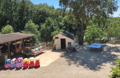 Area giochi vicino a Catus, Occitania, Francia, con macchinine giocattolo, casetta ed alberi rigogliosi.