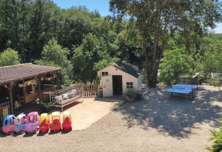 Area giochi vicino a Catus, Occitania, Francia, con macchinine giocattolo, casetta ed alberi rigogliosi.