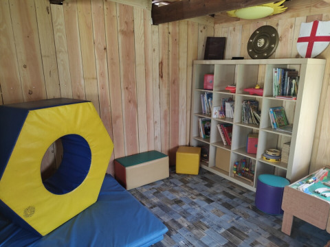 Sala giochi per bambini al campeggio Pagel in Occitania, Francia, con giochi, scaffali e cuscini colorati.