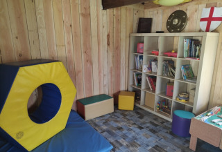 Sala giochi per bambini al campeggio Pagel in Occitania, Francia, con giochi, scaffali e cuscini colorati.