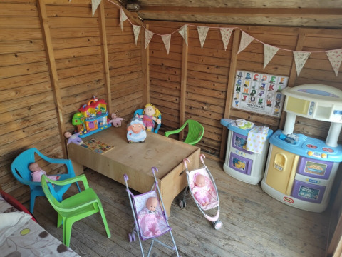 Area gioco per bambini con bambole, cucina giocattolo e sedie colorate in una casetta di legno a Pagel, Occitania.