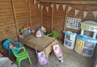 Area gioco per bambini con bambole, cucina giocattolo e sedie colorate in una casetta di legno a Pagel, Occitania.