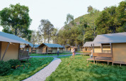 Et moderne glamping-sted med telthytter, gangsti, grønne områder og folk der nyder den friske luft.