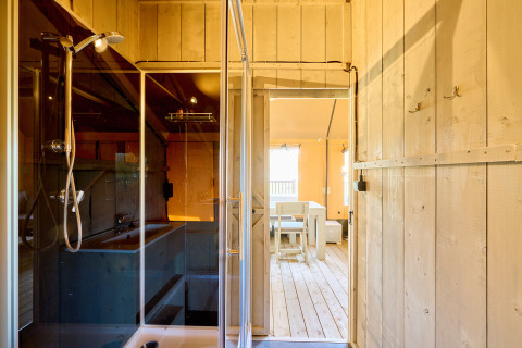 Interno di una tenda safari Ranger al campeggio Spina Family Collection in Italia, con doccia e zona pranzo.