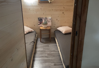 Kleine slaapkamer in safaritent met twee eenpersoonsbedden en houten muren op Camping Des Randonneurs in Frankrijk.