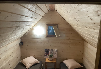 Cozy cabin room with two single beds, wooden walls, small window and light, in a French safari tent.