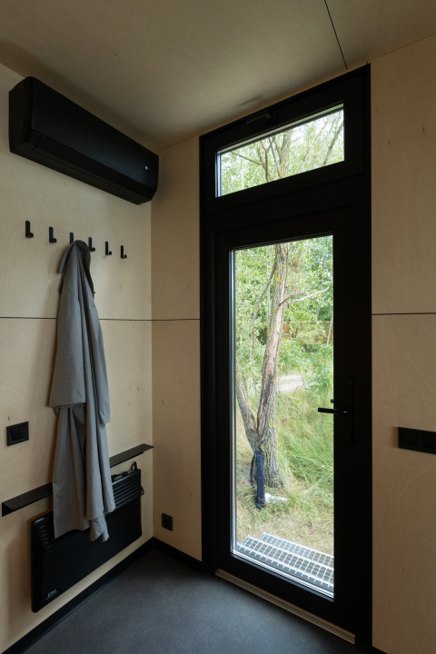Indgang i River Mirrorlodge ved Holiday park Mölke, moderne interiør med frakke og store vinduer.