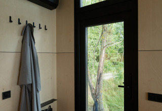 Indgang i River Mirrorlodge ved Holiday park Mölke, moderne interiør med frakke og store vinduer.