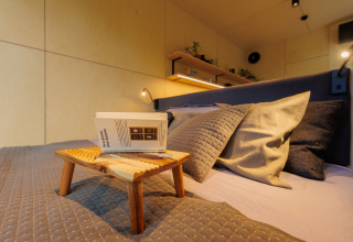 Komfortabel seng med puder, sengebakke og bog på River Mirrorlodge i Holiday park Mölke, Holland.