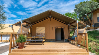 Safari tent Lodge tent Bergerac Deluxe with wooden deck, picnic table, and bench under a clear blue sky.