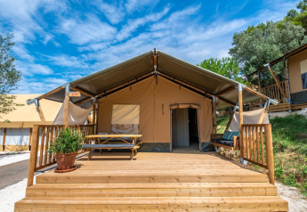 Tenda safari Lodge tent Bergerac Deluxe con terrazza in legno, tavolo da picnic e panca sotto cielo azzurro.
