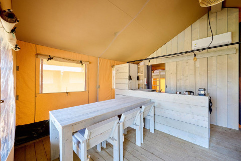 Vista interior de una tienda Safari Cottage con mesa y sillas de madera en Vigna sul Mar Family Camping Village, Italia.