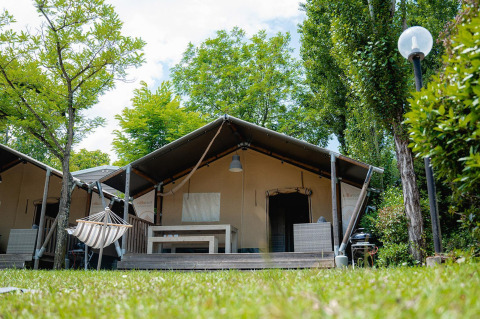Safaritent Villatent Wood op Camping Il Poggetto in Italië, omgeven door bomen en een grasveld.