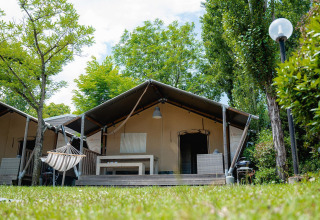Safaritent Villatent Wood op Camping Il Poggetto in Italië, omgeven door bomen en een grasveld.