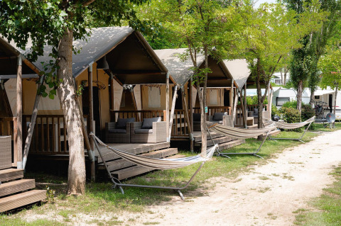 Tende safari con veranda e amache presso Camping Il Poggetto in Italia, circondate da alberi verdi.