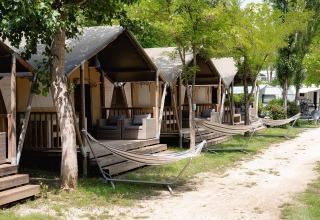Safaritenten met veranda’s en hangmatten bij Camping Il Poggetto in Italië, omgeven door bomen.