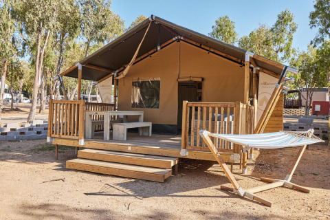 Safaritent met een houten terras, picknicktafel en hangmat bij Villatent Outback, tussen de bomen.